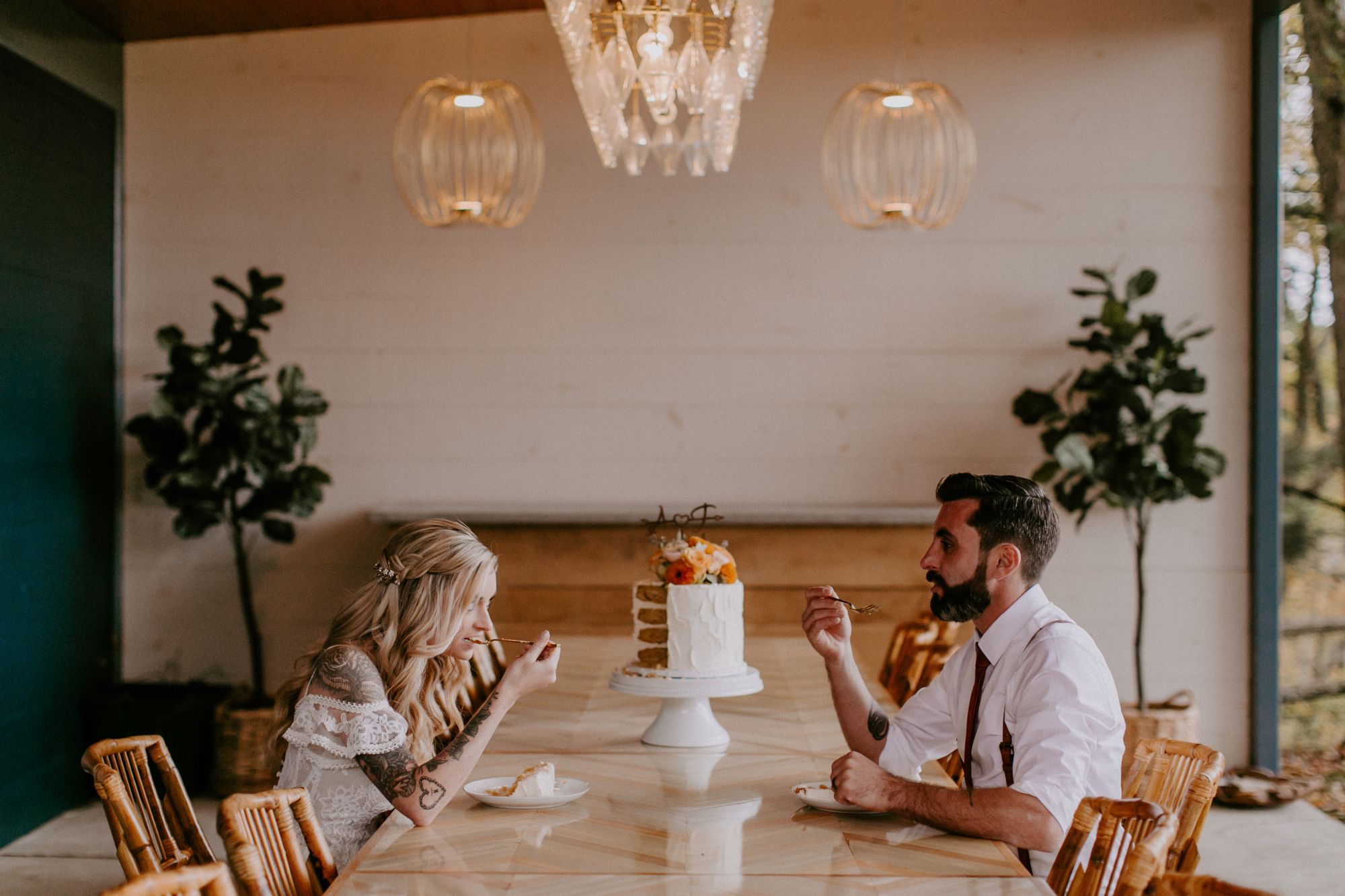 Newlywed bride and groom sitting at a table eating wedding cake.