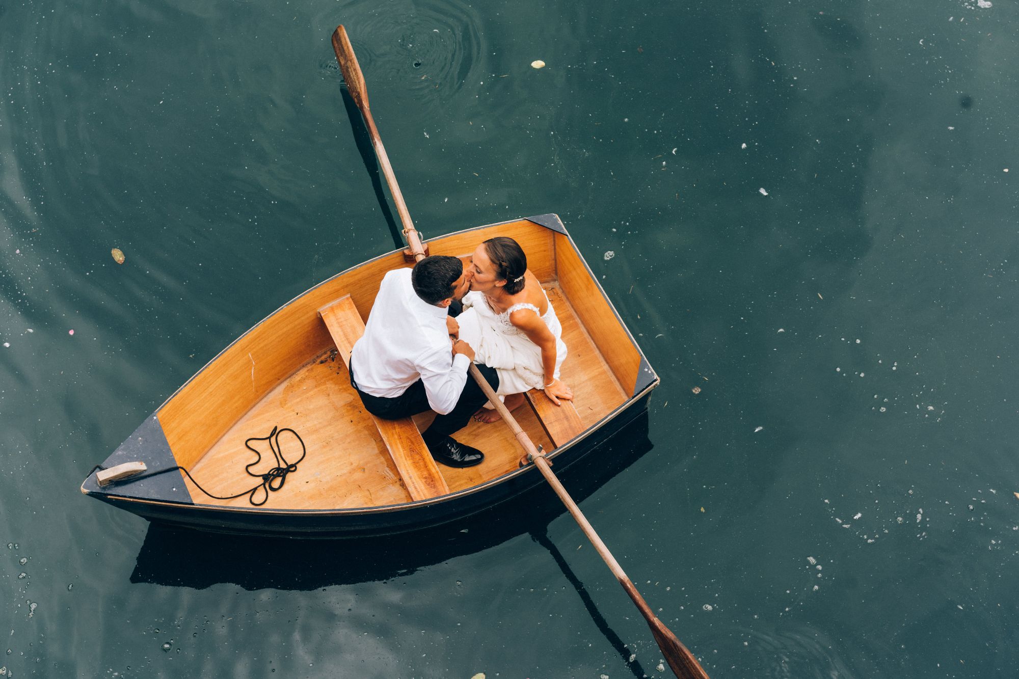 Newlywed couple kissing in row boat.