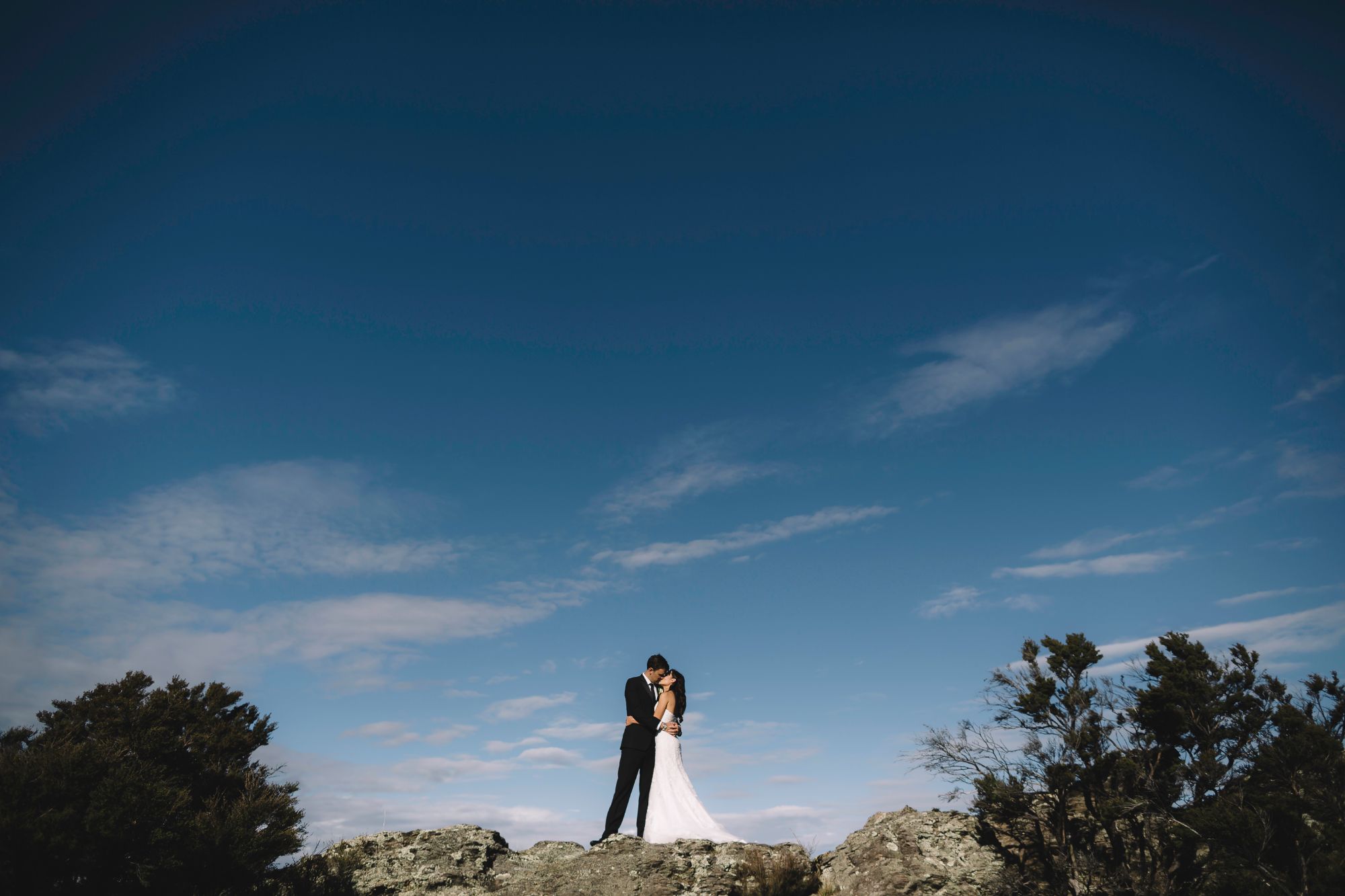 Newlywed couple kissing on clifftop.