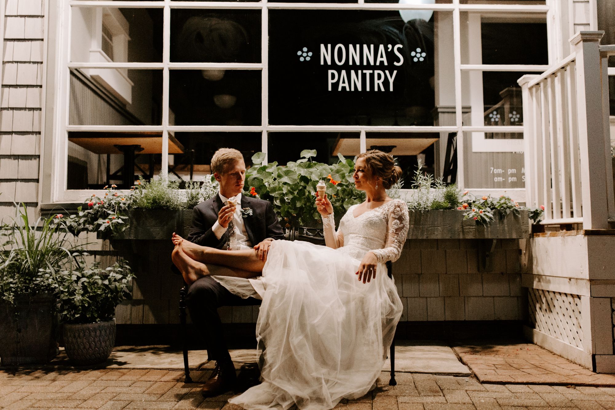 Newlywed bride and groom sitting on a cafe bench eating icecream.