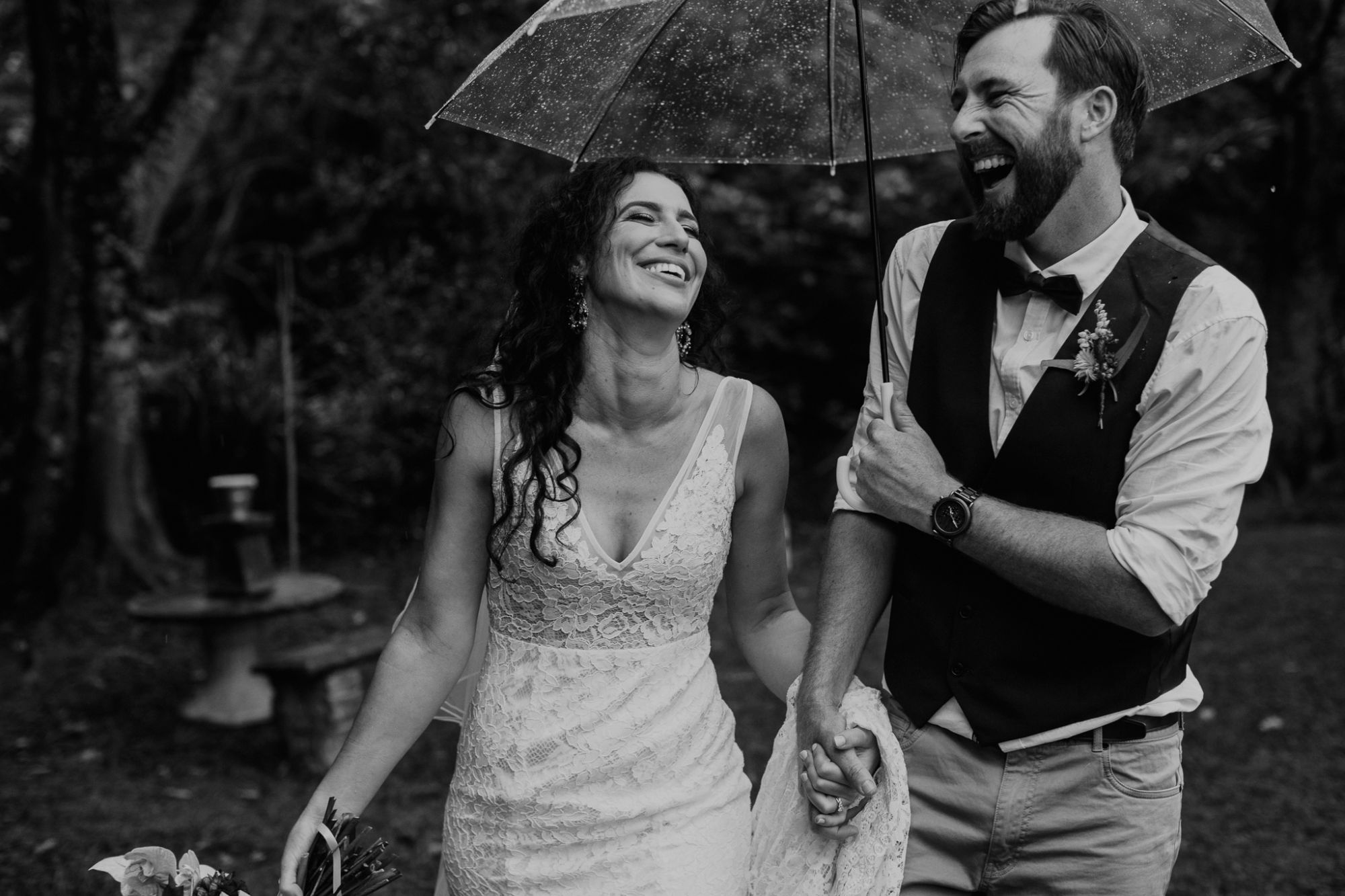 Newlywed bride and groom smiling under an umbrella.