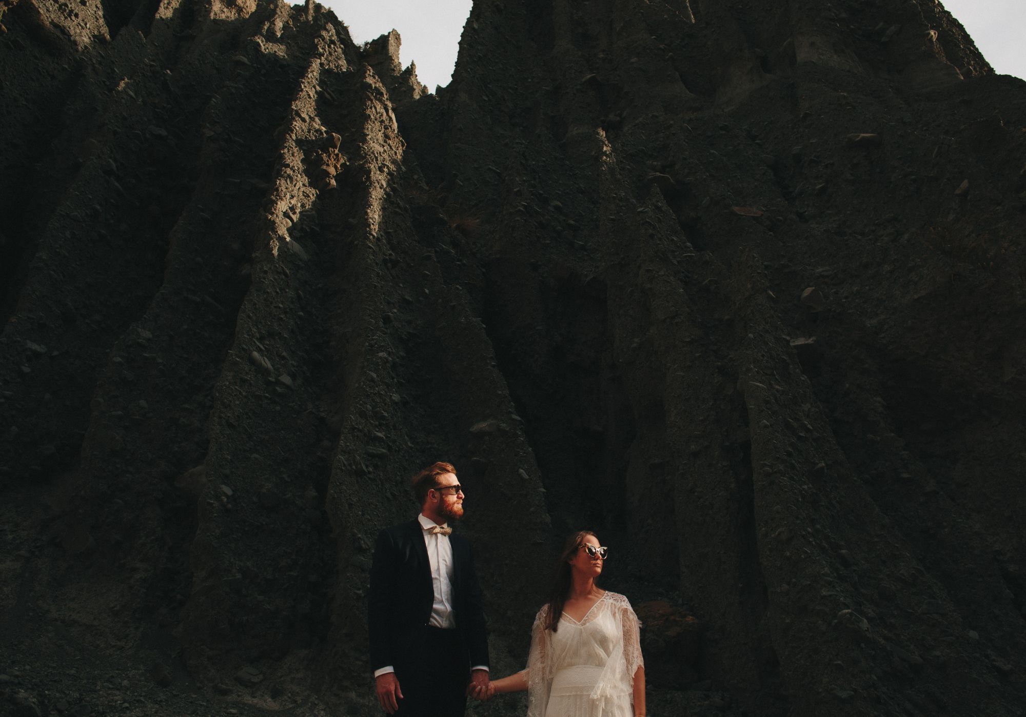 Newlywed couple in sunglasses outdoors by rockface.