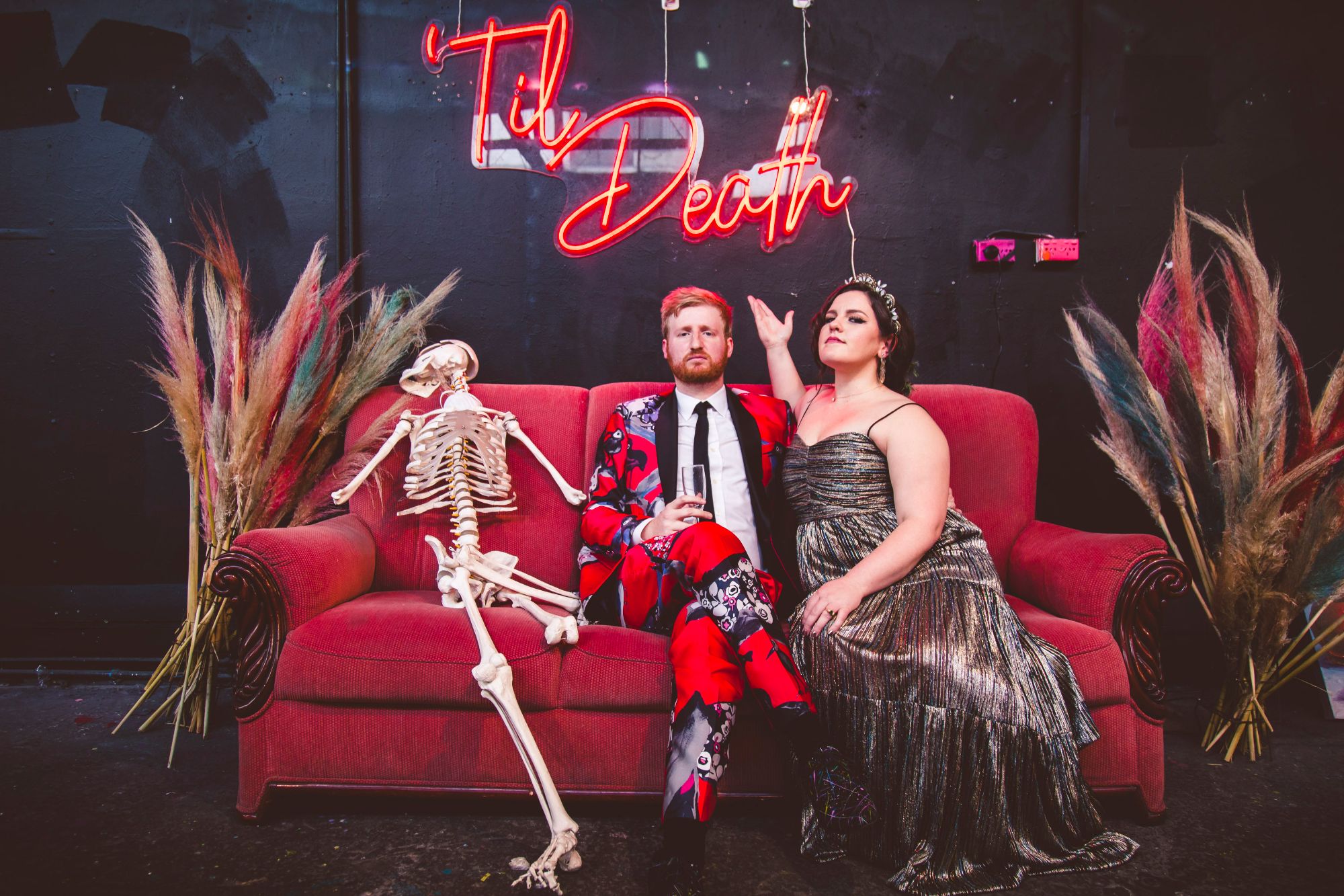 Newlywed couple on red sofa under neon signage.