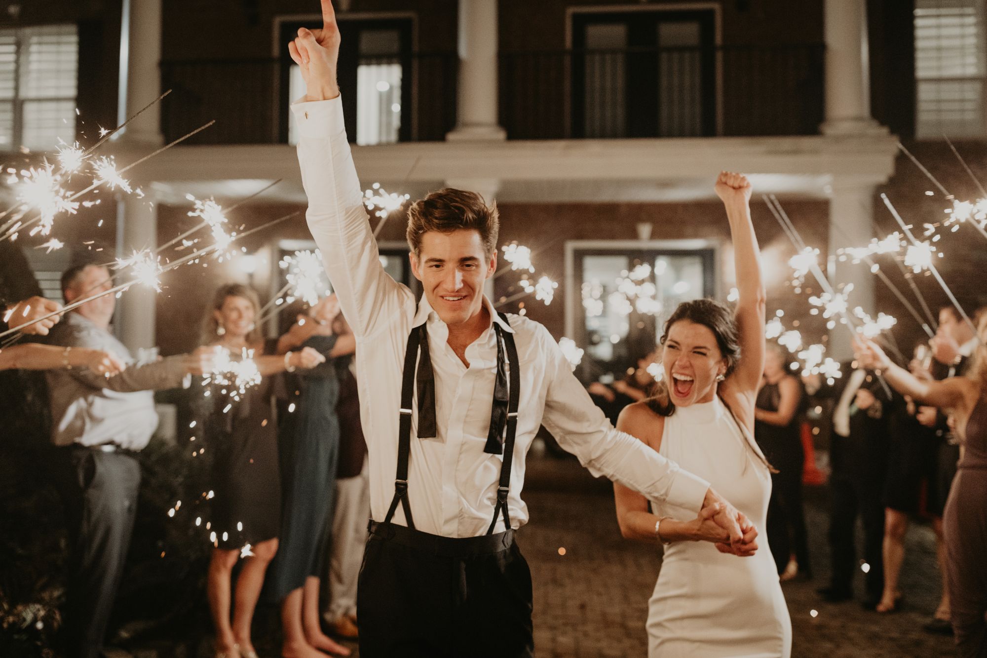 Newlywed couple walking amongst guests holding sparklers.