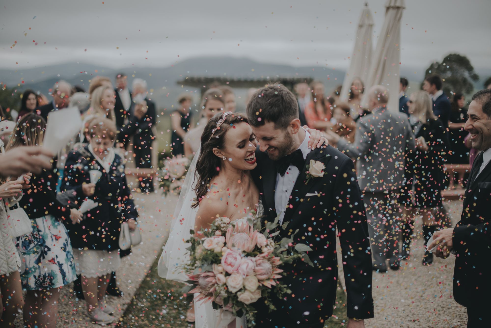 Newlywed couple walking down aisle with confetti being thrown by guests.