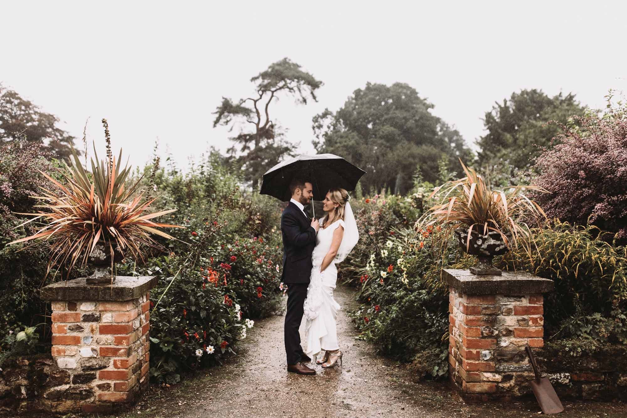 A bride and groom under an umbrella in a garden