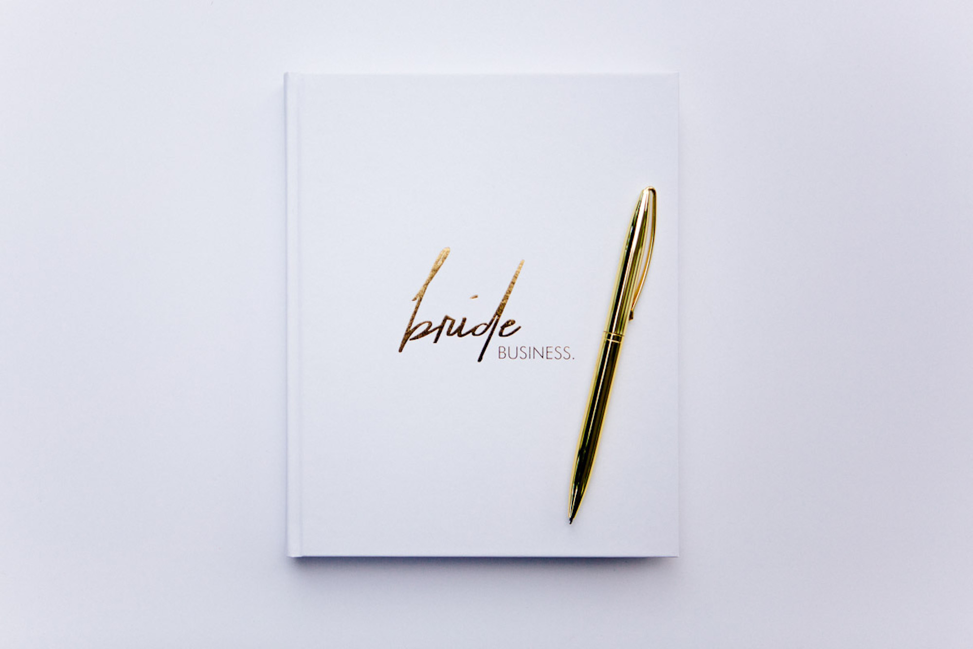 Un cuaderno con la leyenda "bride business" en la portada y un bolígrafo dorado sobre un fondo liso.