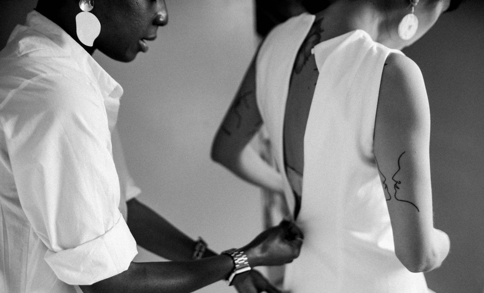 A woman zipping up another woman's white wedding dress
