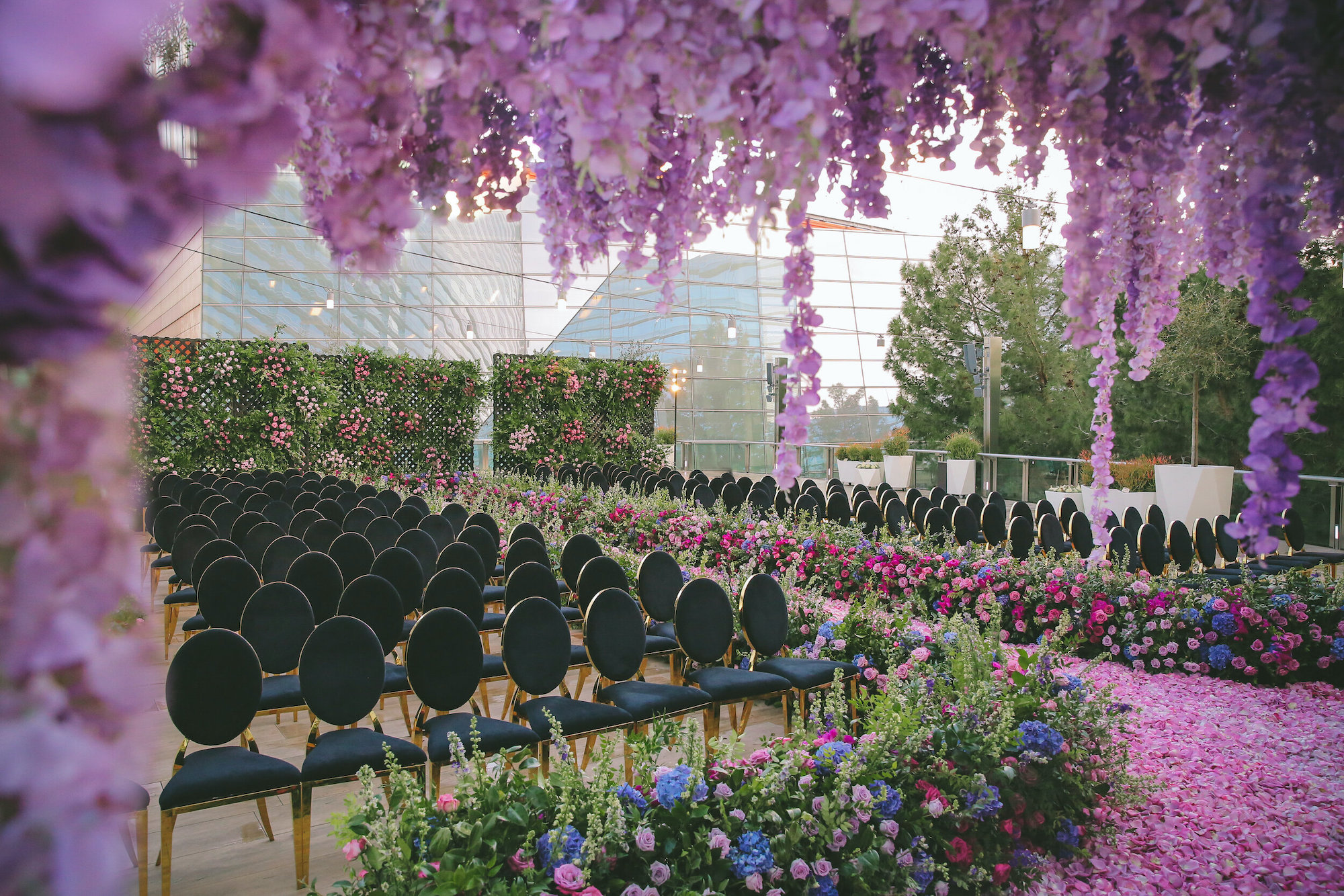A wedding ceremony with rows of black chairs and flowers down the aisle